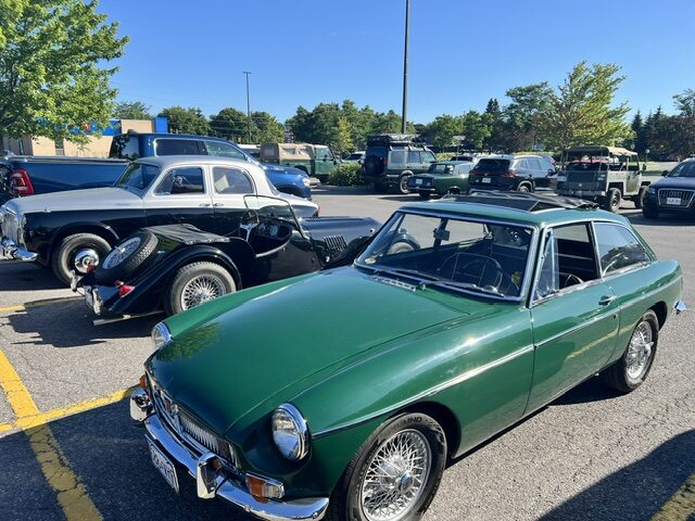 A green MG classic roadster parked on sunny asphalt near Barrhaven Broadways before All British Car Day.
