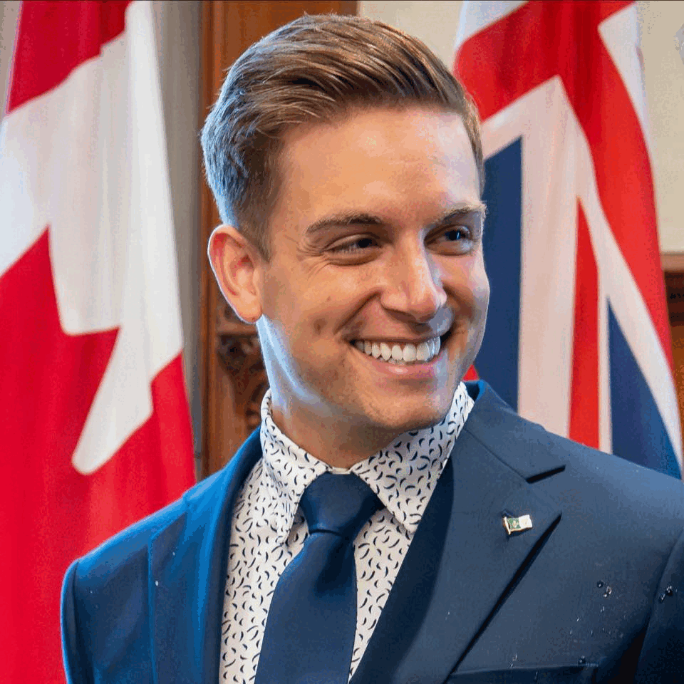 Nepean MPP Tyler Watt in front of Canadian and Ontario flags.