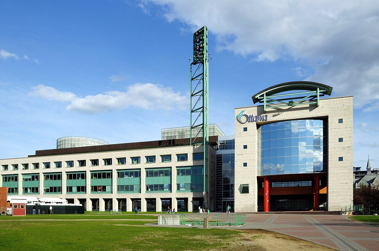 The front of Ottawa City Hall on Laurier Avenue, with its bell tower and Ottawa sign, on a sunny day.