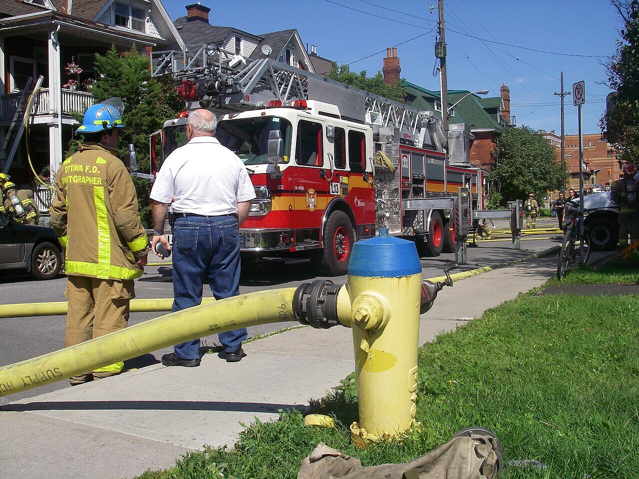 An Ottawa fire crew and ladder truck at a residential call, hose connected to a hydrant.